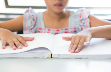 Niña sentada tocando un libro con escritura braille